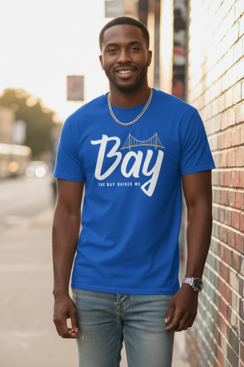 Man wearing a blue t-shirt with 'Bay' printed on it, standing against a brick wall.