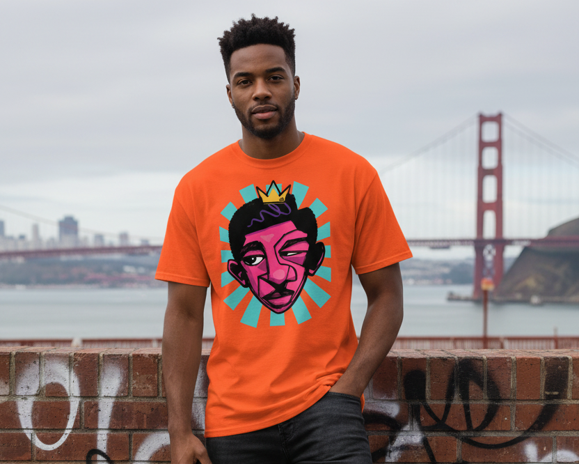 Person wearing an orange t-shirt with a graphic design, standing against a graffiti-covered wall with a bridge in the background.